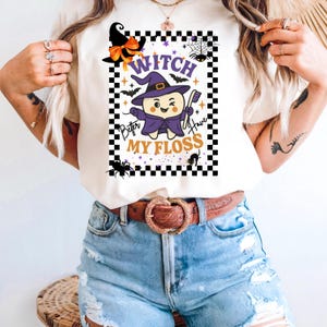 Peut inclure: T-shirt crème avec un motif sur le thème d'Halloween. Le motif représente une dent de dessin animé déguisée en sorcière, tenant une brosse à dents, avec le texte "Witch Better Have My Floss" dans un cadre à carreaux.