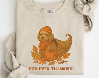 May include: Beige sweatshirt with a graphic of a dog wearing an orange hat and scarf, inside a cornucopia with fall leaves, a pumpkin, and corn. The text "FUR-EVER THANKFUL" is below the graphic.