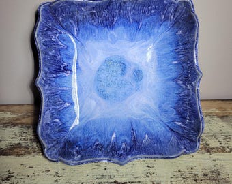 May include: A square ceramic dish with a blue and white glaze. The dish has a scalloped edge and a slightly raised center.