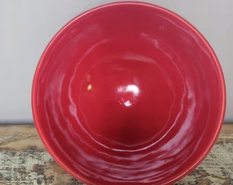 May include: A round, deep bowl with a vibrant, glossy red interior and exterior finish. The surface of the bowl features a subtle, wavy, and rippled texture throughout, creating a series of concentric circular indentations along the inner walls.