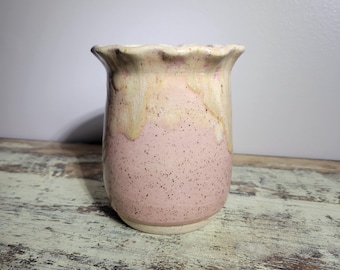 May include: A small, pink and white ceramic vase with a scalloped rim. The vase has a speckled glaze and a light pink base.