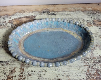 May include: A light blue ceramic oval dish with a beaded rim. The dish has a speckled glaze and a slightly raised center.