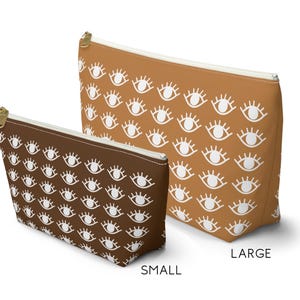 May include: Two cosmetic bags with a white eye pattern on a brown and tan background. The smaller bag is brown and the larger bag is tan. The text "SMALL" is below the smaller bag and "LARGE" is below the larger bag.
