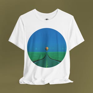 May include: White t-shirt featuring a circular graphic of a hot air balloon flying over a road in a green field with a blue sky.