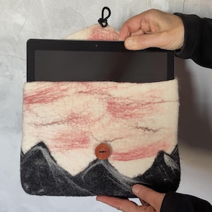 Op de afbeelding: Een witte en roze tablet hoes van vilt met een zwart berglandschap en een houten knoop. De hoes heeft een zwarte draagriem.