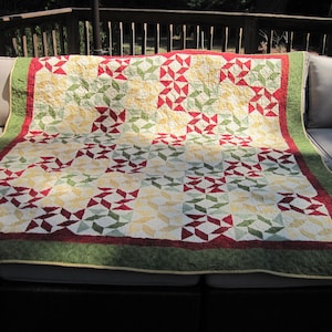 May include: A red, green, and yellow quilt with a geometric pattern. The quilt is folded and placed on a patio furniture set.