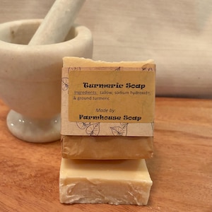May include: A bar of turmeric soap wrapped in brown paper with a label that reads "Turmeric Soap" and "Ingredients: tallow, sodium hydroxide, & ground turmeric" and "Made by: Farmhouse Soap".
