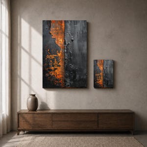 Peut inclure: Deux &oelig;uvres d'art murales abstraites. La plus grande est un rectangle vertical avec une surface noire textur&eacute;e et des accents orange. La plus petite pi&egrave;ce reprend le design. Les deux sont mont&eacute;es sur un mur de ton neutre au-dessus d'un meuble en bois.