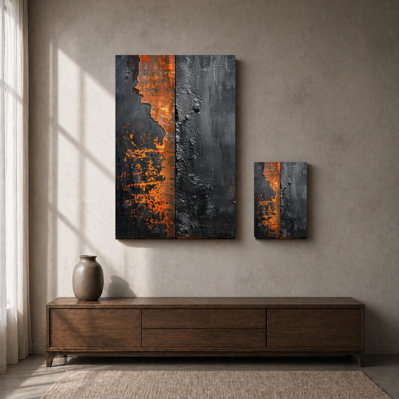 Peut inclure: Deux &oelig;uvres d'art murales abstraites. La plus grande est un rectangle vertical avec une surface noire textur&eacute;e et des accents orange. La plus petite pi&egrave;ce reprend le design. Les deux sont mont&eacute;es sur un mur de ton neutre au-dessus d'un meuble en bois.