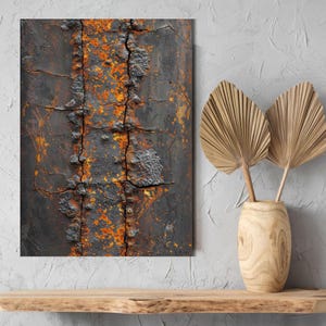 May include: Abstract art print featuring a close-up of weathered metal. The artwork displays a dark, textured surface with orange and yellow rust accents. Cracks and rivets add to the industrial aesthetic. The print is displayed on a wooden shelf with a vase of dried palm leaves.