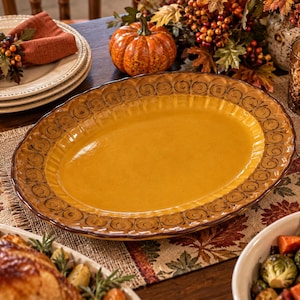 May include: An oval ceramic serving platter with a smooth, mustard-yellow center and a wide, scalloped rim featuring a dark brown, hand-painted spiral pattern. The platter has a glossy finish and a raised, textured edge design.