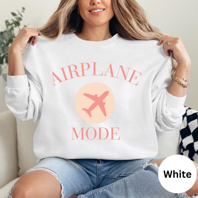 White colored crewneck sweatshirt. Light pink letters in large all caps that read AIRPLANE MODE. Airplane graphic printed in middle of the shirt. Model is wearing an oversized fit. Various colors and sizes available. Perfect cozy sweatshirt for anyone in vacay mode, or gift for a traveler.