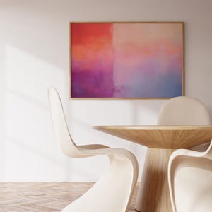 May include: A wooden table with a light wood finish and a rounded top. Three white chairs surround the table. A framed abstract painting with pink, orange, and blue hues hangs on the wall behind the table.