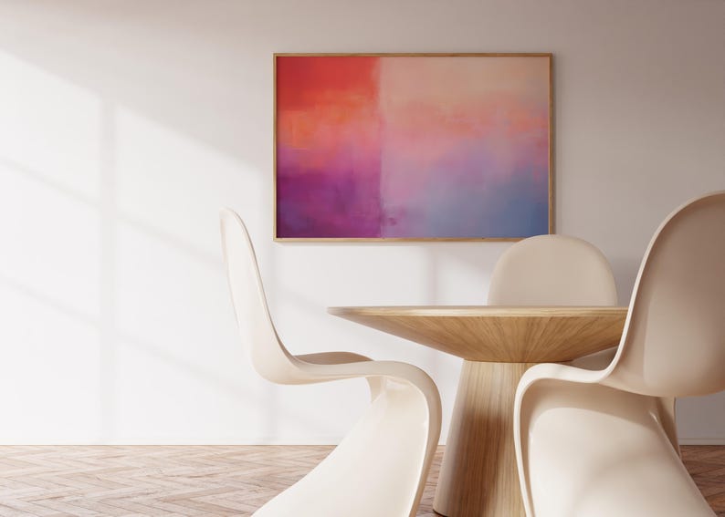 May include: A wooden table with a light wood finish and a rounded top. Three white chairs surround the table. A framed abstract painting with pink, orange, and blue hues hangs on the wall behind the table.