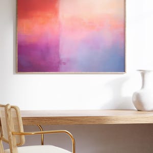 May include: Abstract painting in a wooden frame with a pink, orange, and blue color scheme. The painting is hanging on a white wall above a wooden desk and chair.
