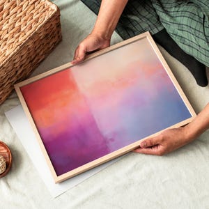 May include: A framed abstract painting with a gradient of orange, pink, purple, and blue colors. The painting is in a light wood frame.