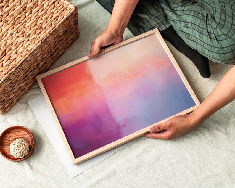 May include: A framed abstract painting with a gradient of orange, pink, purple, and blue colors. The painting is in a light wood frame.