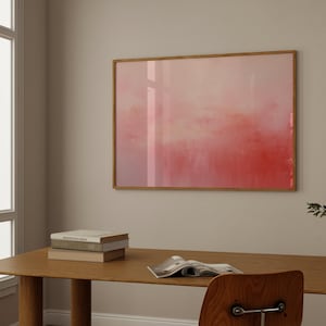 May include: A framed abstract painting with a pink and orange gradient. The painting is hanging on a white wall above a wooden desk with a stack of books and a magazine.