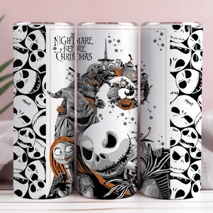 May include: A white tumbler featuring a design from "The Nightmare Before Christmas." The design includes Jack Skellington, Sally, and other characters in grayscale with orange accents. The tumbler has a repeating skull pattern.