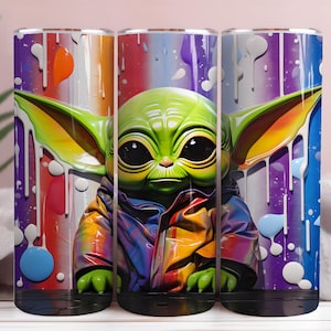 May include: Three cylindrical tumblers with a colourful design of a green alien character. The artwork features paint drips and a rainbow background. The tumblers are designed to hold liquids and are suitable for everyday use.