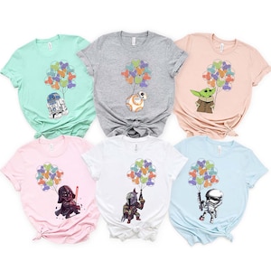May include: Six different t-shirts featuring various Star Wars characters holding colorful balloons. The characters include Darth Vader, a Mandalorian, a Stormtrooper, R2-D2, BB-8, and Baby Yoda.