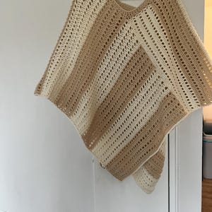 May include: A crocheted poncho with brown and white stripes. The poncho is made from lightweight yarn and has a loose, flowing fit.