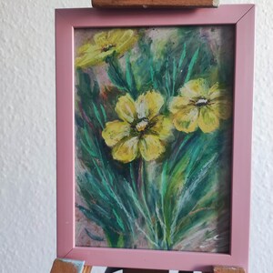 Könnte beinhalten: Gerahmtes Gemälde mit gelben Blumen und grünen Blättern, in einem rosa Rahmen auf einer Holzstaffelei. Das Kunstwerk hat einen impressionistischen Stil mit sichtbaren Pinselstrichen. Die Staffelei ist aus Holz.