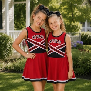 May include: Two sleeveless red cheerleading dresses featuring black and white diagonal stripes across the chest and the word SPIRIT printed in white block letters. Each dress has a flared skirt with a white and black hem and a black hair bow.