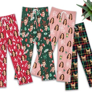 Op de afbeelding: Vier paar pyjamabroeken met verschillende patronen. Eén paar is rood met gezichten en kerstontwerpen, een ander is groen met gezichten en zuurstokken, een derde is roze met gezichten en sneeuwvlokken, en de laatste is geruit met hondengezichten.