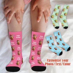 Op de afbeelding: Roze sokken met een herhalend cartoonkarakterontwerp, een rode hoed en een schop. De tekst "Custom Text Here" is op de sokken gedrukt. Extra sokken met een Groot-ontwerp en blauwe sokken met een cartoonkarakterontwerp worden ook getoond. De tekst "Customize your Photo/Text/Color" wordt ook weergegeven.