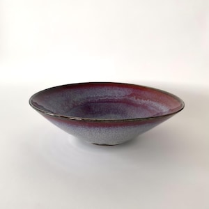 Peut inclure: Un bol en céramique de conception large et peu profonde. Le bol présente un dégradé de couleurs, passant d'un bord bordeaux foncé à un intérieur gris clair avec une touche de violet. Le bord est de couleur marron foncé.