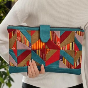 May include: A teal zippered clutch with a patchwork design featuring geometric shapes in shades of red, orange, yellow, brown, and purple.