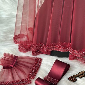 Pu&ograve; includere: Velo da sposa color borgogna con bordino perlato, fascia in raso color borgogna abbinata con bordino perlato e un paio di maniche in tulle color borgogna con bordino perlato.