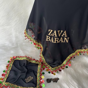 Puede incluir: Pañuelo negro y pañuelo cuadrado a juego con texto bordado en oro "ZAVA BARAN". Ambos artículos tienen un ribete dorado, rojo y verde con detalles de lentejuelas de colores. Los artículos se exhiben sobre una superficie blanca y esponjosa.