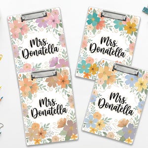 Könnte beinhalten: Vier Klemmbretter mit floralen Designs in Pastellfarben. Jedes Klemmbrett trägt den Namen "Mrs. Donatella" in schwarzer Schrift. Die floralen Arrangements umfassen rosa, orange, blaue und gelbe Blumen mit grünen Blättern.