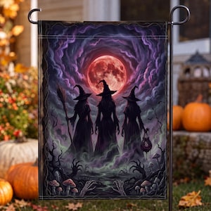 May include: A rectangular garden flag featuring a dark, atmospheric scene of three silhouetted figures in pointed hats standing before a large, glowing red moon. The foreground includes skeletal hands, mushrooms, and swirling purple and green mist.