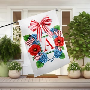 Puede incluir: Una bandera de jardín blanca con un lazo rojo, blanco y azul, amapolas rojas, hortensias azules y banderas americanas que rodean un escudo verde y azul con la letra "A" en rojo.