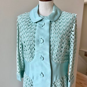 May include: A light blue dress with a lace overlay and a peter pan collar. The dress has a button-up front and three buttons.