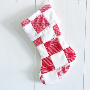 May include: A red and white patchwork Christmas stocking with a variety of patterns. The stocking is made of fabric and has a white cuff.