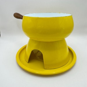 May include: Yellow enamel fondue pot with a wooden handle and a matching yellow base. The pot has a white interior.