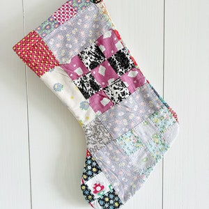 May include: A patchwork Christmas stocking made from various fabrics in shades of pink, red, blue, green, and white. The stocking is quilted and has a traditional stocking shape.