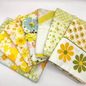 May include: A collection of vintage floral bed sheets in various colors, including yellow, white, and green. The sheets feature daisy and floral patterns. Some sheets have lace trim.