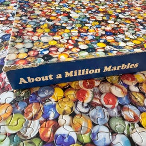 May include: A partially assembled jigsaw puzzle featuring a colorful array of marbles. The puzzle box, with the title "About a Million Marbles," is visible. The marbles are in various colors, including red, yellow, blue, and green.