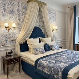 Könnte beinhalten: Ein luxuriöses Schlafzimmer mit einem Himmelbett, einem marineblauen Kopfteil und einem passenden Bettrand. Die Bettwäsche umfasst weiße Kissen und eine blau-weiß gemusterte Tagesdecke. Die Wände sind mit blau-weißer Blumentapete verziert.