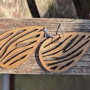 May include: A pair of wooden earrings with a zebra stripe pattern. The earrings are shaped like teardrops and have silver hooks.