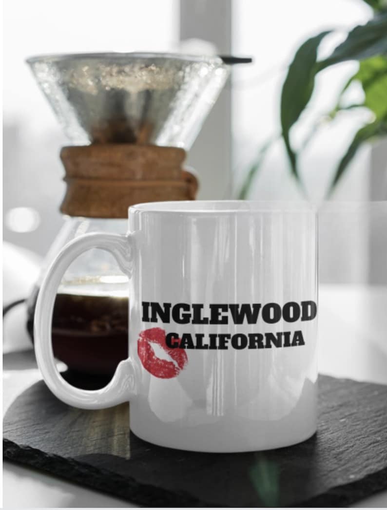 Może przedstawiać: Biały kubek ceramiczny z czarno-białym nadrukiem z napisem "INGLEWOOD CALIFORNIA" i czerwonym śladem po szmince.
