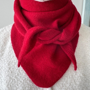 May include: A vibrant red triangular scarf with a knitted texture, wrapped and knotted around the neck of a mannequin. The scarf features a soft, fuzzy appearance and is draped to form a point at the front, layered over a white textured garment.