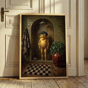 May include: A framed wall art print depicting a yellow frog wearing a dark shower cap while standing in a tiled shower stall. A patterned towel hangs on the wall, a potted plant sits on the floor, and a checkered rug lies on the wooden floor.