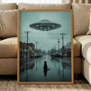 Op de afbeelding: Ingelijste kunstprint met een regenachtige straatscène met een UFO erboven. Een zwarte kat zit in de natte straat en weerspiegelt de lichten van de UFO. Het kunstwerk toont een oldtimer en een vrachtwagen, en elektriciteitsleidingen.