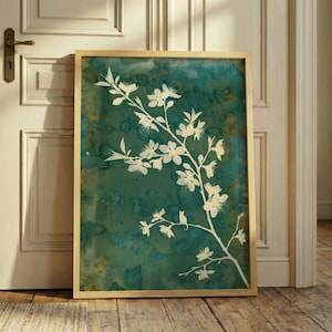 Pode incluir: Uma impressão de arte emoldurada com uma silhueta de ramo floral branco contra um fundo de aquarela verde e turquesa. A obra de arte está em uma moldura de madeira clara e está encostada em uma porta branca e um chão de madeira.